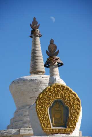 Two ornate white stupas with intricate golden decorations stand under a clear blue sky, the moon visible in the background—an enchanting scene perfect for tourism and travel enthusiasts exploring Mongolia.
