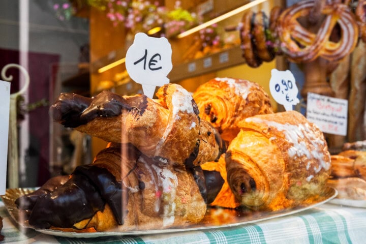 A display of pastries, including some chocolate-dipped, graces the bakery window in France, each with a price tag showing costs in euros.