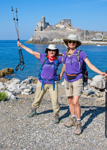 Two women in hiking outfits smiling and posing next to the Ligurian coast and in front of Palmaria Island in the Tuscany region of Italy