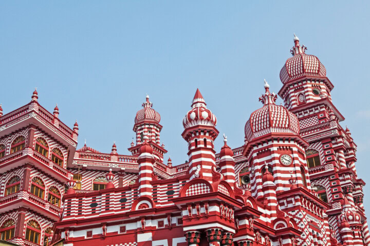 The red and white candy-striped building with ornate towers and domes against a clear blue sky is reminiscent of the vibrant architecture found in Sri Lanka.
