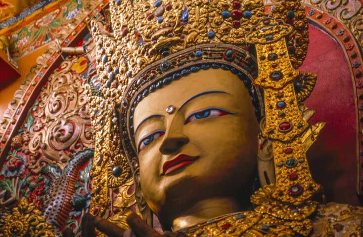 A close-up of an ornate golden statue adorned with colorful gemstones, depicting a deity with intricate details and a serene expression, set against a vibrant decorative background inspired by Nepalese artistry.