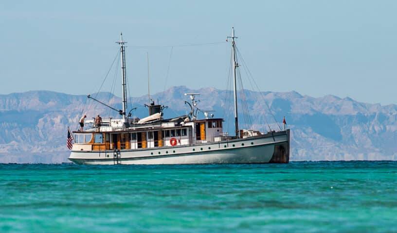 A vintage boat anchored in the clear turquoise waters of Mexico, with a backdrop of stunning mountains under a crystal-clear sky.