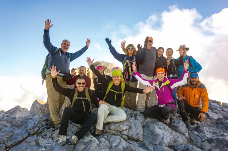 Group of people on top of mountain with hands up.
