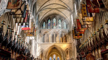 Explore the interior of a gothic cathedral in Dublin, showcasing high vaulted ceilings, stunning stained glass windows, and colorful flags adorning the upper walls—truly a must-see destination for travel enthusiasts seeking captivating things to do.