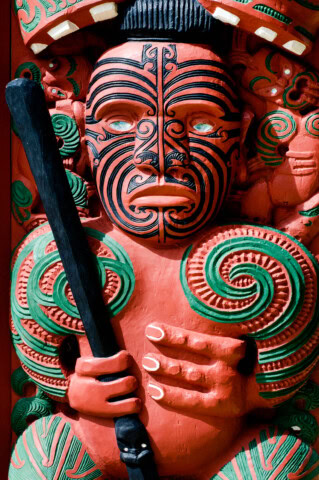 Maori carving of a tattooed figure holding a staff, richly decorated with green and red patterns, showcasing the rich cultural heritage of New Zealand.