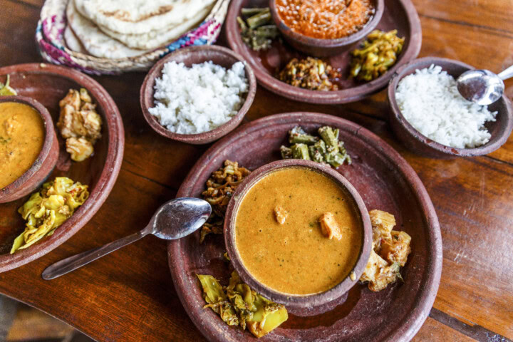 A table set with bowls of Sri Lankan curry, rice, vegetables, and sauces on wooden plates, accompanied by spoons and flatbread.