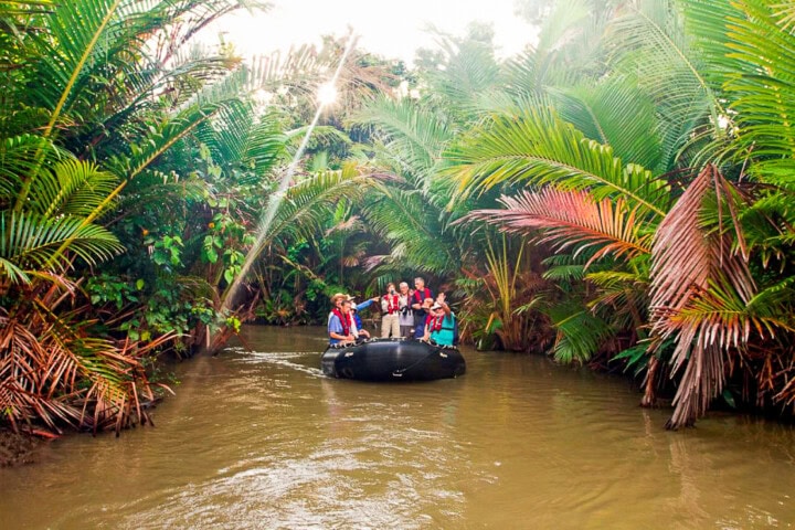 A group of people in life jackets are rafting on a river surrounded by lush green tropical vegetation in Papua New Guinea.